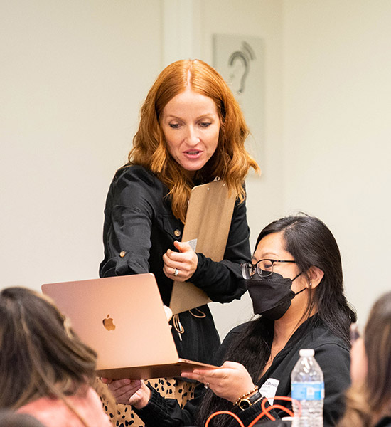 Vanessa Errecarte teaching a group of students as she points at a student laptop and discusses with them